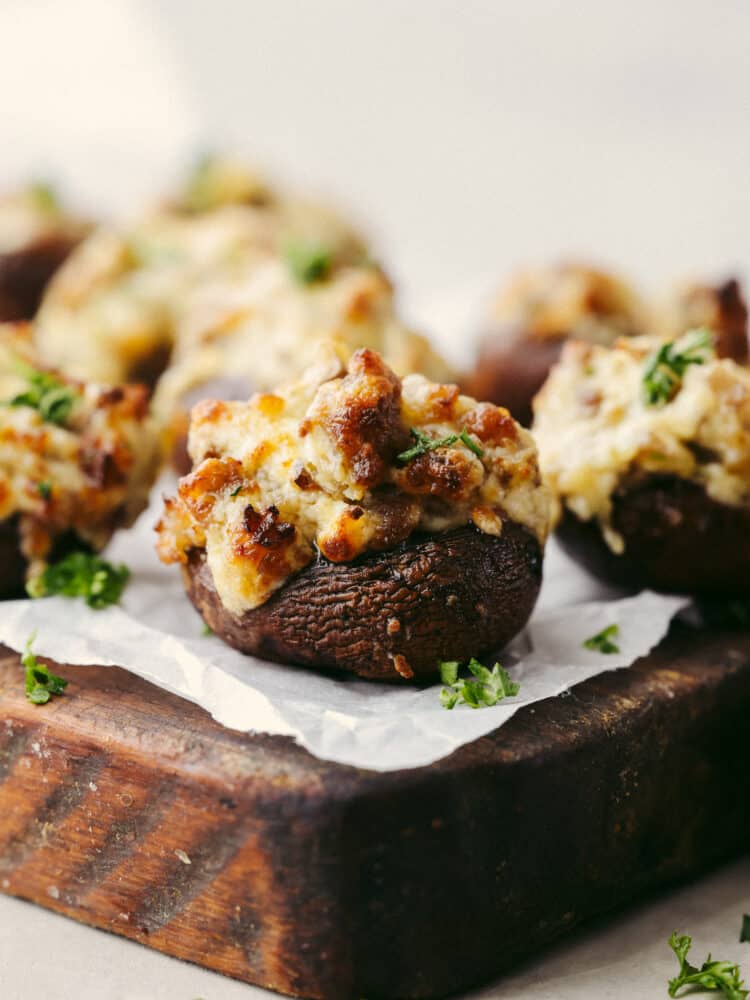 The perfect bite-sized appetizer, air fryer sausage stuffed mushrooms are hearty and meaty with a flavorful sausage filling your family won't be able to get enough of! They work great as both an appetizer and a side dish to complement your favorite meals! Closeup of a sausage stuffed pepper on a serving board.