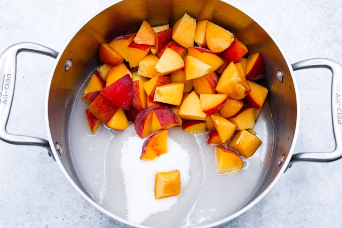 This is the absolute BEST fresh peach lemonade recipe! Sweet juicy peaches combined with tart, tangy lemons make the most refreshing drink. You will want to have a pitcher of this in your fridge throughout the peach season! overhead shot of peaches with sugar and water in