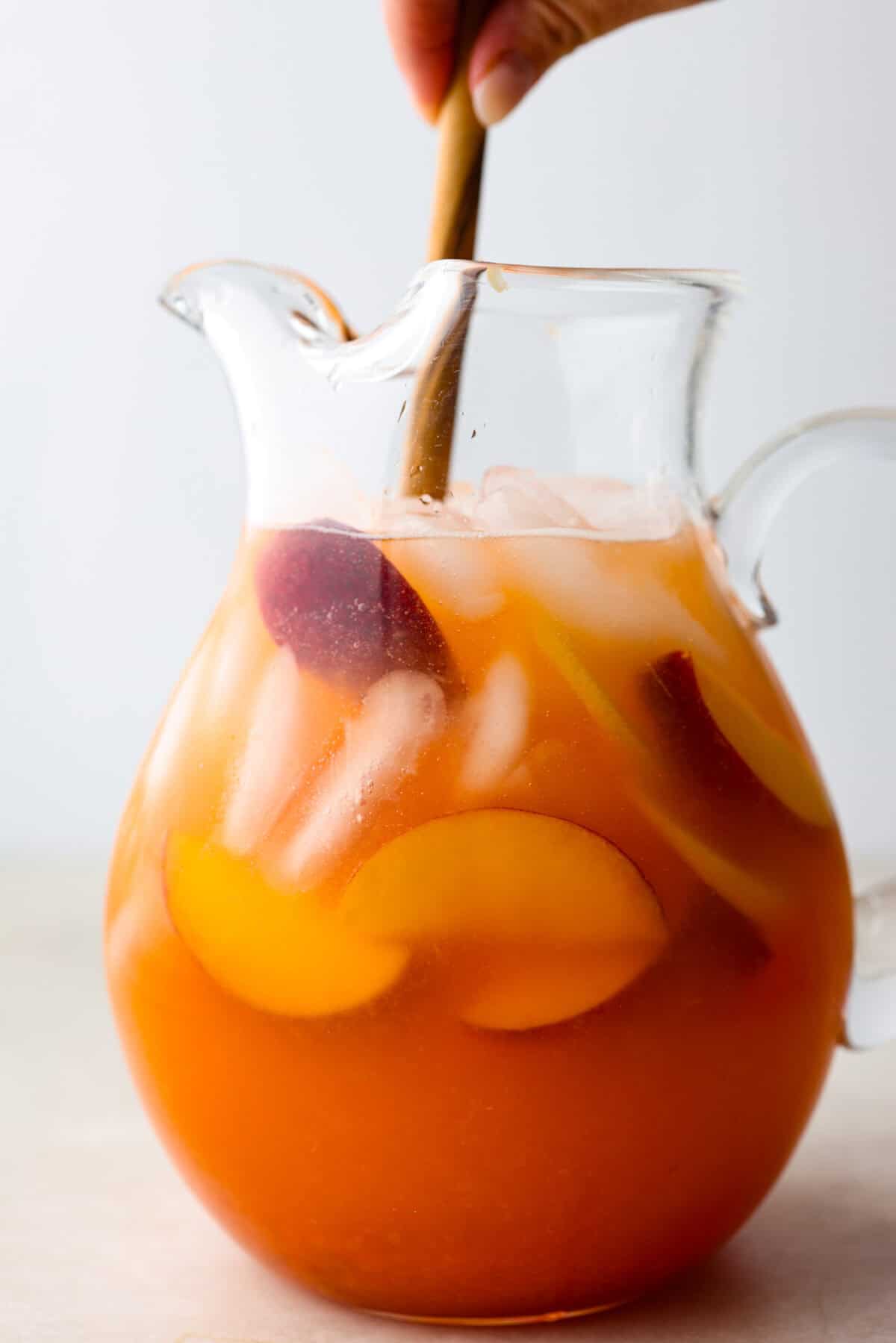 This is the absolute BEST fresh peach lemonade recipe! Sweet juicy peaches combined with tart, tangy lemons make the most refreshing drink. You will want to have a pitcher of this in your fridge throughout the peach season! Side shot of pitcher of lemonade with someone stirring with a wooden spoon.