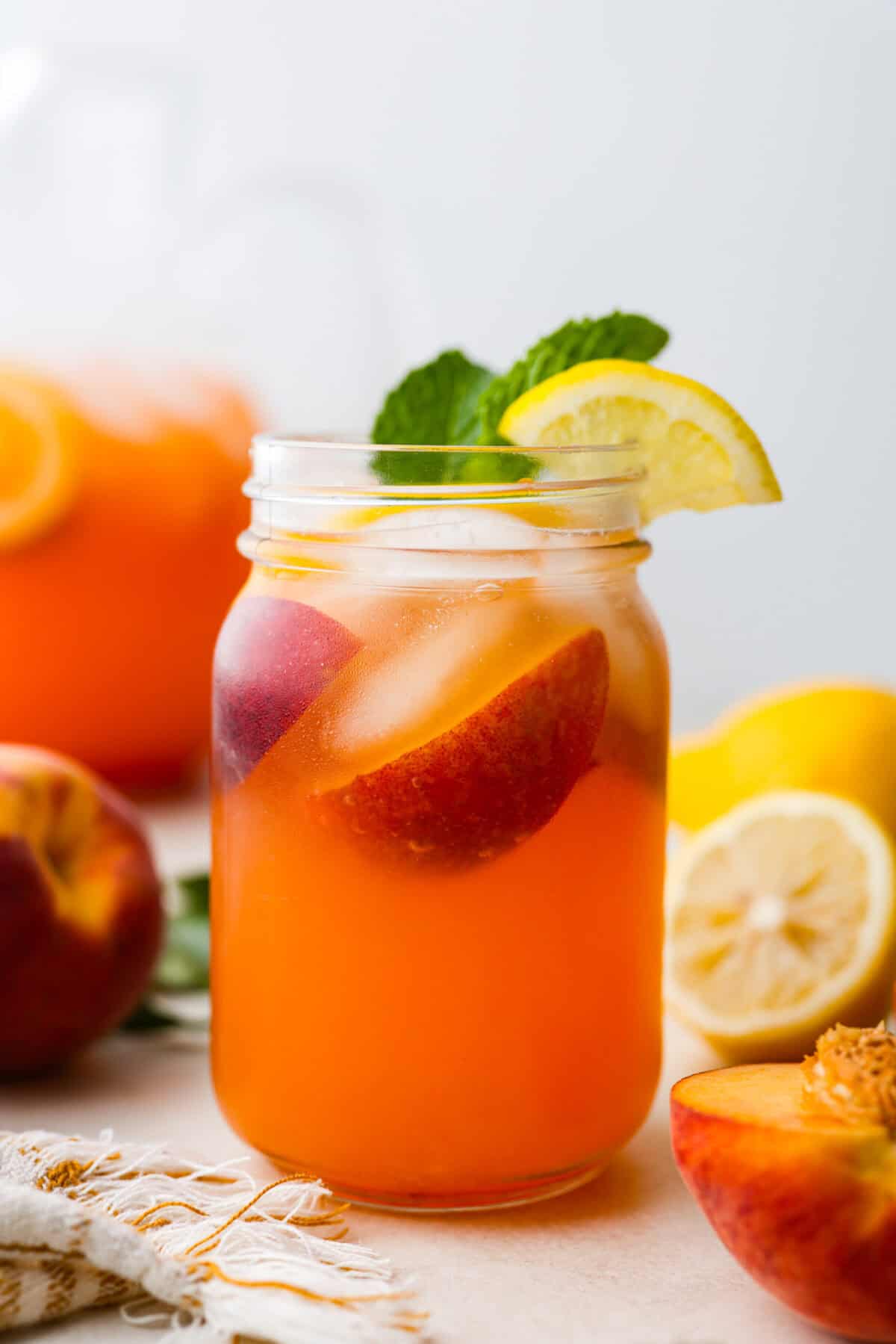 This is the absolute BEST fresh peach lemonade recipe! Sweet juicy peaches combined with tart, tangy lemons make the most refreshing drink. You will want to have a pitcher of this in your fridge throughout the peach season! Side shot of mason jar with fresh peach lemonade with sprig of mint and garnished with a wedge of lemon.