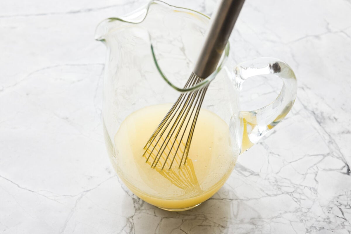 Someone stilling lemon juice and sugar in a large pitcher. 