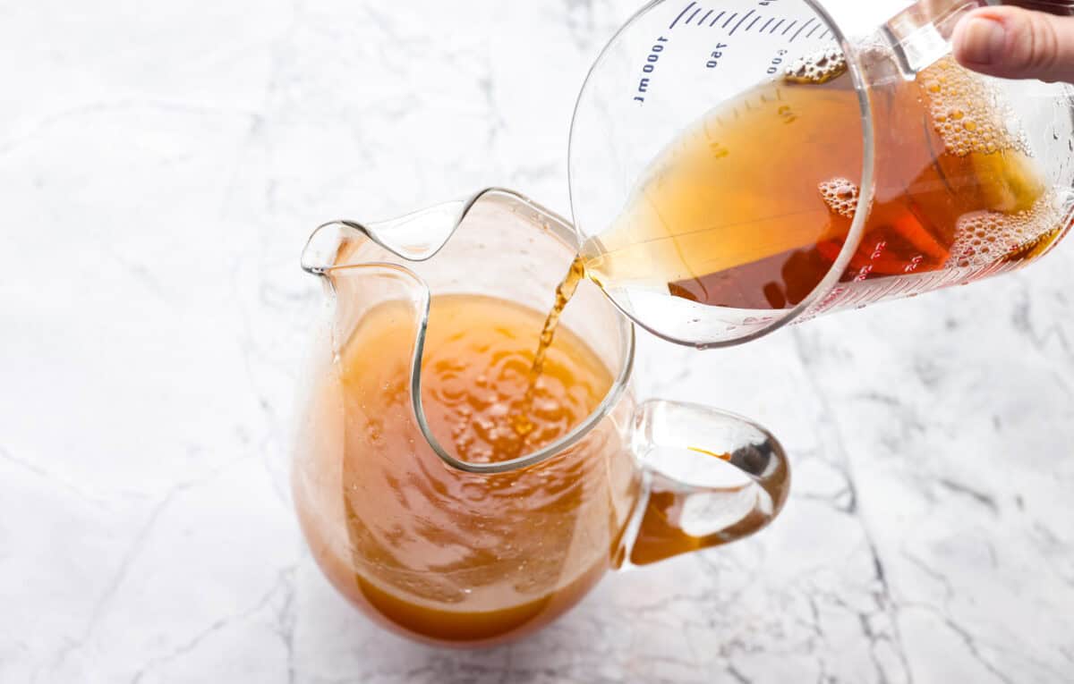 Someone pouring unsweetened black tea into the pitcher with lemon juice and sugar. 