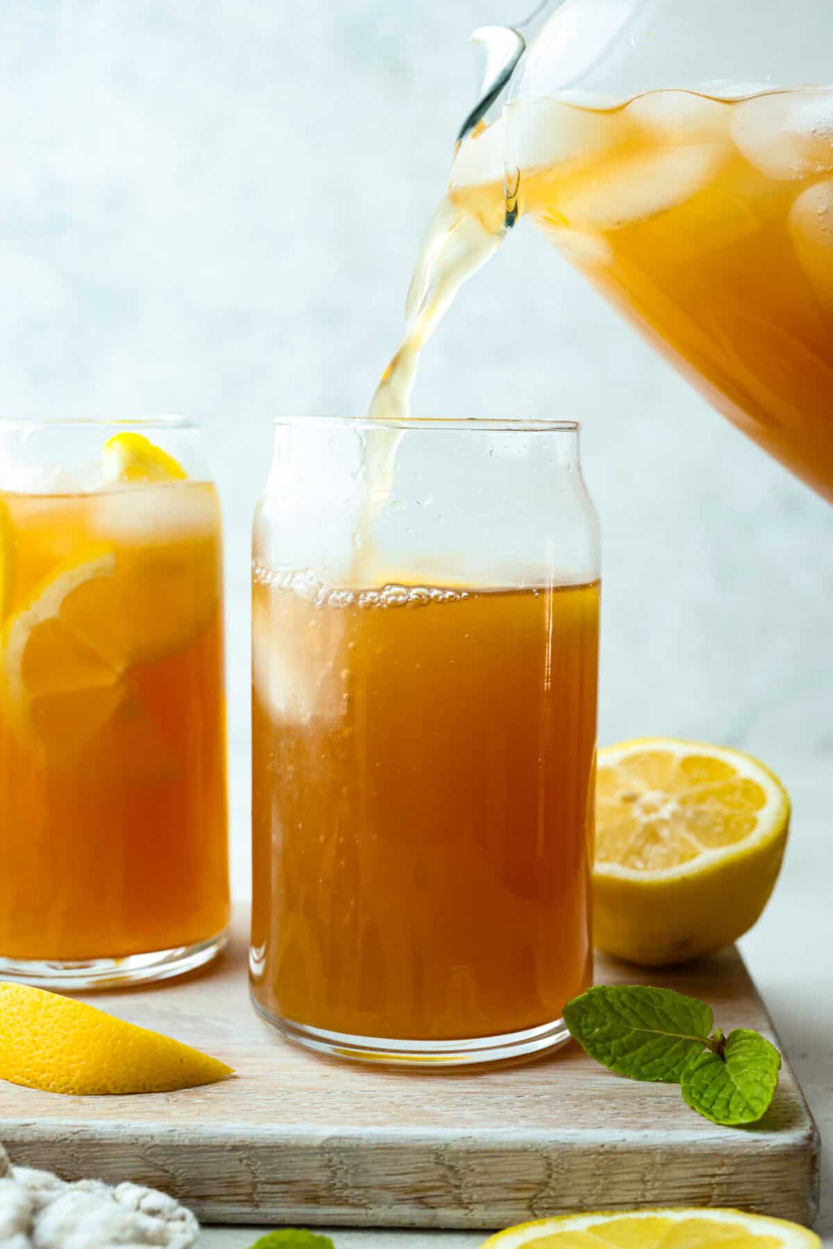 Someone pouring Arnold Palmer mix into a tall glass with ice and lemon slices. 